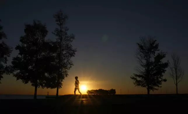 FILE - A man runs in silhouette on a bike path in the Bronzeville neighborhood of Chicago, as the sun rises over Lake Michigan on Oct. 17, 2024. (AP Photo/Charles Rex Arbogast, File)