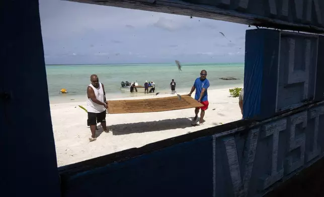 Brian Fidiiy and Ray Marino, the governor of Hatohobei State, carry lumber to the ranger station for maintenance repairs on Helen Island, Palau, July 17, 2024. (AP Photo/Yannick Peterhans)