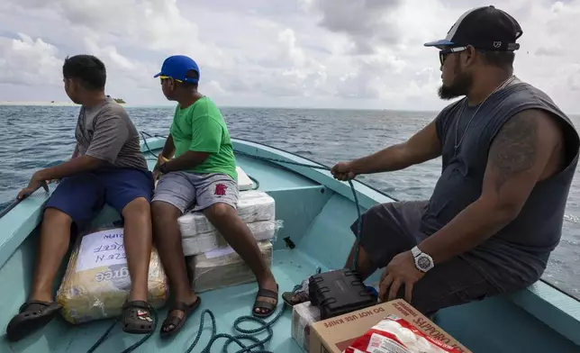 Metfidza Marino, from left, Aarson Aaron and Aaron Cyrillo look out to Helen Island, Palau, as a small speed boat transports toilet paper, dog food and other goods to the remote atoll on July 17, 2024. (AP Photo/Yannick Peterhans)