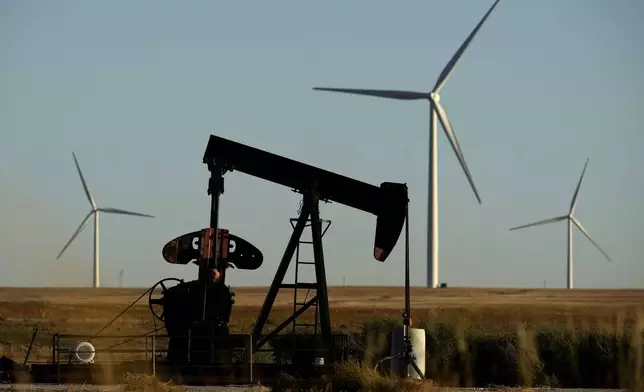 A pumpjack operates in the foreground while wind turbines at the Buckeye Wind Energy wind farm work in the distance, Monday, Sept. 30, 2024, near Hays, Kan. (AP Photo/Charlie Riedel)