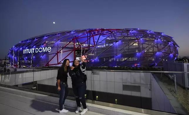 Two fans take a selfie outside the Intuit Dome, the new home of the Los Angeles Clippers, before the team's NBA preseason basketball game against the Dallas Mavericks Monday, Oct. 14, 2024, in Inglewood, Calif.(AP Photo/Jae C. Hong)