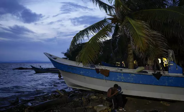 Venezuelan migrant Kilver Rengifo looks at his phone while waiting to cross the Gulf of Uraba to walk across the Darien Gap ,in an attempt to reach the U.S., in Necocli, Colombia, Sunday, Oct. 13, 2024. (AP Photo/Matias Delacroix)