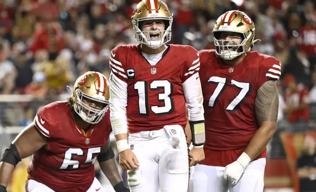 San Francisco 49ers quarterback Brock Purdy (13) celebrates after scoring a touchdown with guard Aaron Banks, left, and guard Dominick Puni (77) during the second half of an NFL football game against the Dallas Cowboys in Santa Clara, Calif., Sunday, Oct. 27, 2024. (AP Photo/Eakin Howard)