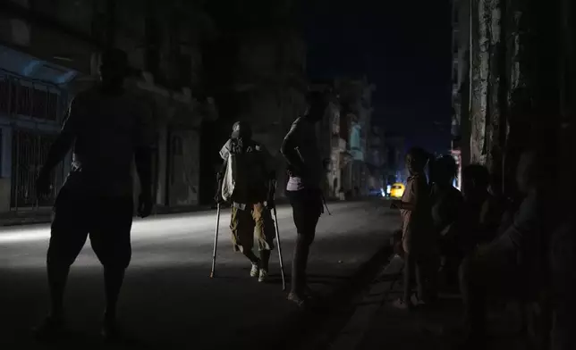 A man walks along a street with the aid of crutches during a massive blackout after a major power plant failed in Havana, Cuba, Friday, Oct. 18, 2024. (AP Photo/Ramon Espinosa)