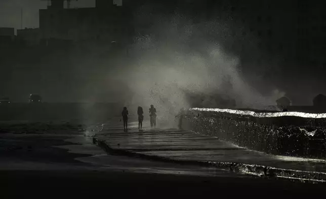People walk along the boardwalk as waves crash during a power outage in Havana, Monday, Oct. 21, 2024. (AP Photo/Ramon Espinosa)