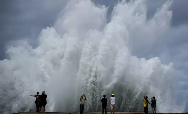 People take photos of the spray from waves crashing against the Malecon seawall, brought by the tail end of Hurricane Milton, in Havana, Cuba, Wednesday, Oct. 9, 2024. (AP Photo/Ramon Espinosa)