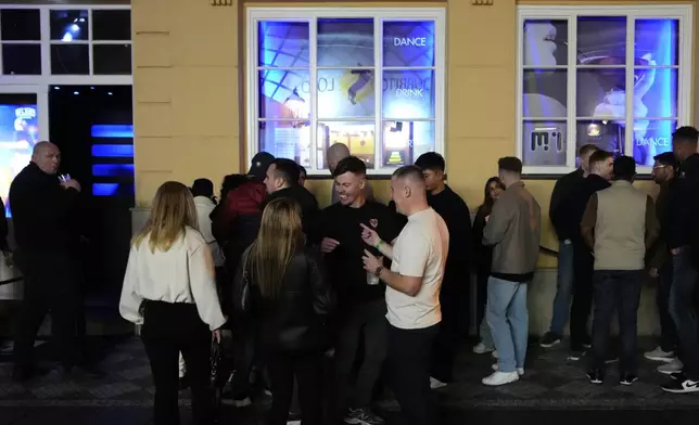 A group of tourists stand in line outside a bar as they attend a pub crawl tour in downtown Prague, Czech Republic, Thursday, Oct. 17, 2024. (AP Photo/Petr David Josek)