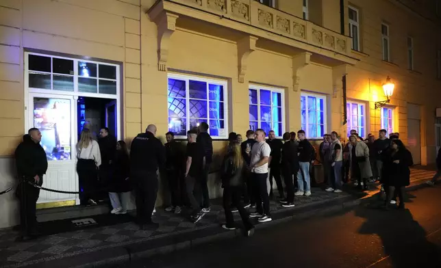 A group of tourists stand in line outside a bar as they attend a pub crawl tour in downtown Prague, Czech Republic, Thursday, Oct. 17, 2024. (AP Photo/Petr David Josek)