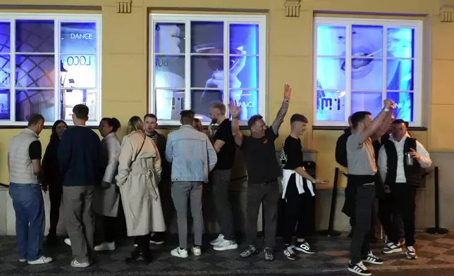 A group of tourists stand in line outside a bar as they attend a pub crawl tour in downtown Prague, Czech Republic, Thursday, Oct. 17, 2024. (AP Photo/Petr David Josek)