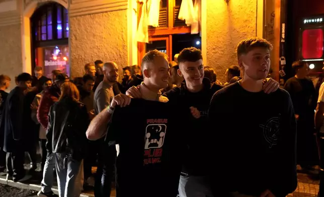 A group of tourists stand in line outside a bar as they attend a pub crawl tour in downtown Prague, Czech Republic, Thursday, Oct. 17, 2024. (AP Photo/Petr David Josek)