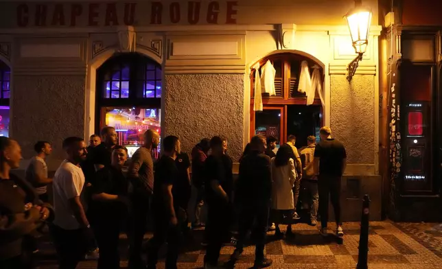 A group of tourists stand in line outside a bar as they attend a pub crawl tour in downtown Prague, Czech Republic, Thursday, Oct. 17, 2024. (AP Photo/Petr David Josek)