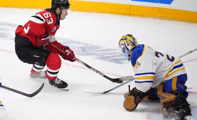 New Jersey Devils' Jesper Bratt, left, skates past Buffalo Sabres' Devon Levi during the NHL hockey game between Buffalo Sabres and New Jersey Devils, in Prague, Czech Republic, Saturday, Oct. 5, 2024. (AP Photo/Petr David Josek)