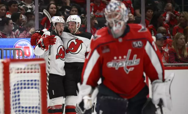 New Jersey Devils center Paul Cotter, left, celebrates his goal with right wing Stefan Noesen, center as Washington Capitals goaltender Charlie Lindgren (79) looks on at right during the second period of an NHL hockey game, Saturday, Oct. 12, 2024, in Washington. (AP Photo/Nick Wass)