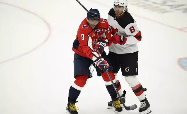 Washington Capitals left wing Alex Ovechkin, left, battles for the puck against New Jersey Devils defenseman Johnathan Kovacevic, right, during the third period of an NHL hockey game, Saturday, Oct. 12, 2024, in Washington. (AP Photo/Nick Wass)