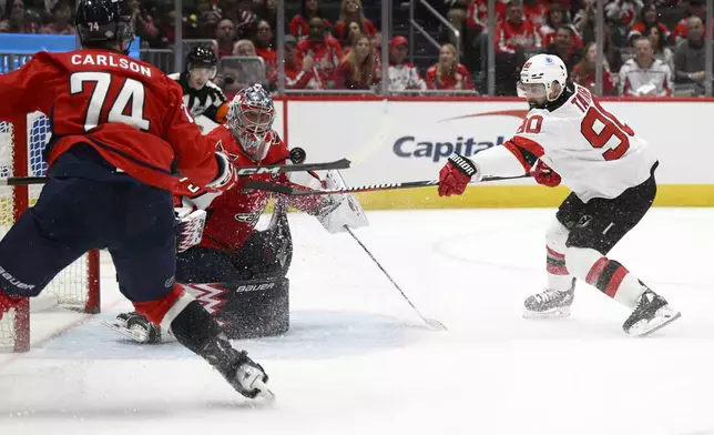 New Jersey Devils left wing Tomas Tatar (90) tries to get the puck past Washington Capitals goaltender Charlie Lindgren, center, and defenseman John Carlson (74) during the second period of an NHL hockey game, Saturday, Oct. 12, 2024, in Washington. (AP Photo/Nick Wass)