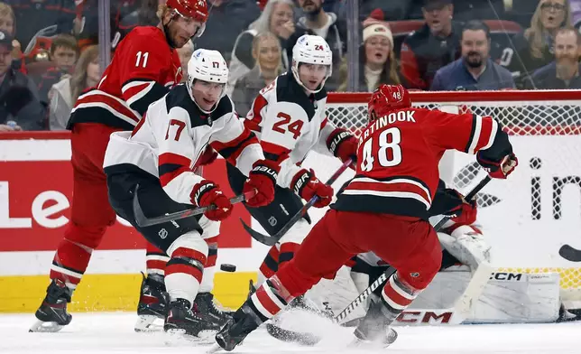 New Jersey Devils' Simon Nemec (17) and Seamus Casey (24) watch the shot by Carolina Hurricanes' Jordan Martinook (48) with Hurricanes' Jordan Staal (11) nearby during the third period of an NHL hockey game in Raleigh, N.C., Tuesday, Oct. 15, 2024. (AP Photo/Karl B DeBlaker)