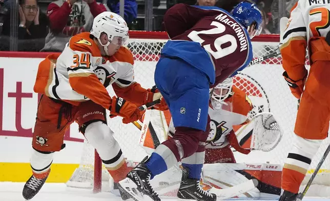 Colorado Avalanche center Nathan MacKinnon (29) shoots the puck for the winning goal as Anaheim Ducks goaltender Lukas Dostal, back right, and defenseman Pavel Mintyukov, left, cover in overtime of an NHL hockey game Friday, Oct. 18, 2024, in Denver. (AP Photo/David Zalubowski)