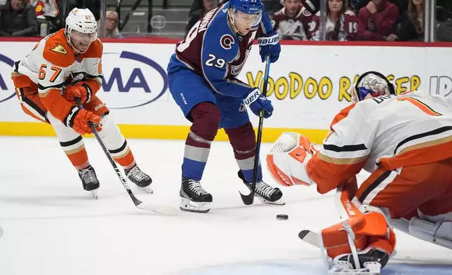 Colorado Avalanche center Nathan MacKinnon, center, drives past Anaheim Ducks defenseman Tristan Luneau, left, to shoot against Ducks goaltender Lukas Dostal, right, in the third period of an NHL hockey game Friday, Oct. 18, 2024, in Denver. (AP Photo/David Zalubowski)