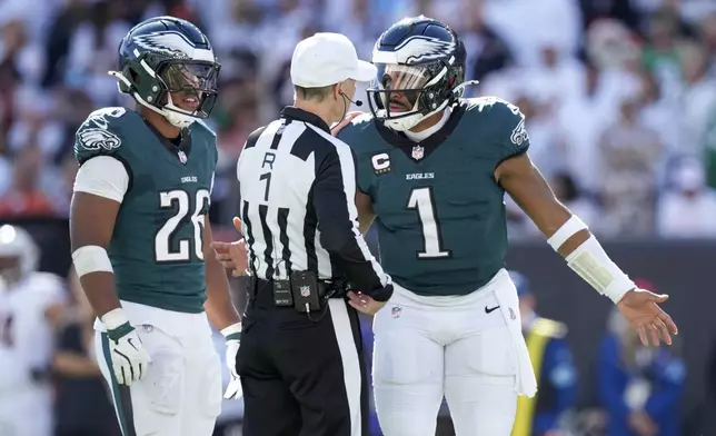 Philadelphia Eagles quarterback Jalen Hurts, right, talks to referee Scott Novak (1) as running back Saquon Barkley (26) looks on during the first half of an NFL football game against the Cincinnati Bengals, Sunday, Oct. 27, 2024 in Cincinnati. (AP Photo/Carolyn Kaster)