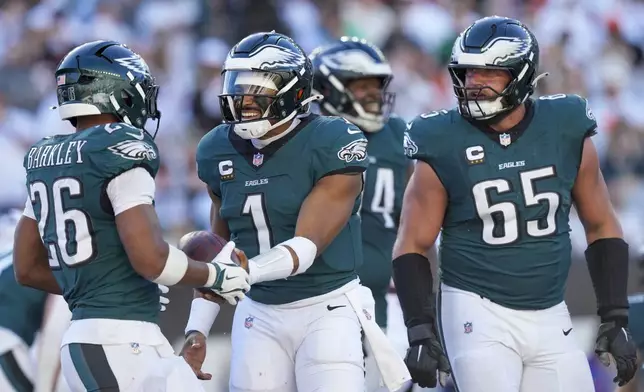 Philadelphia Eagles quarterback Jalen Hurts (1) hands the ball to running back Saquon Barkley (26) after Hurts scored a touchdown against the Cincinnati Bengals during the second half of an NFL football game, Sunday, Oct. 27, 2024 in Cincinnati. Eagles' Lane Johnson (65) looks on. The Eagles won 37-17. (AP Photo/Carolyn Kaster)