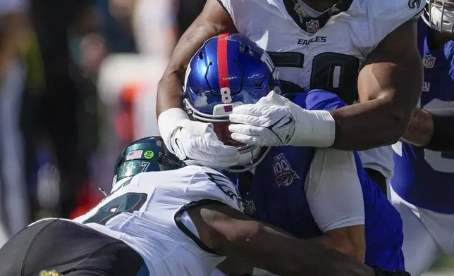 New York Giants quarterback Daniel Jones (8) is sacked by Philadelphia Eagles defensive tackle Thomas Booker IV (59) and linebacker Nakobe Dean (17) during the second quarter of an NFL football game, Sunday, Oct. 20, 2024, in East Rutherford, N.J. (AP Photo/Seth Wenig)