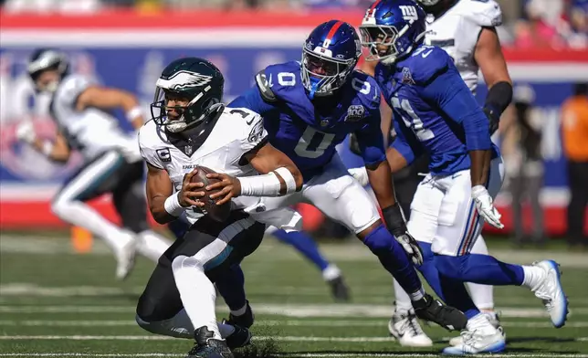 Philadelphia Eagles quarterback Jalen Hurts (1) avoids New York Giants linebacker Brian Burns (0) during the second quarter of an NFL football game, Sunday, Oct. 20, 2024, in East Rutherford, N.J. (AP Photo/Frank Franklin II)