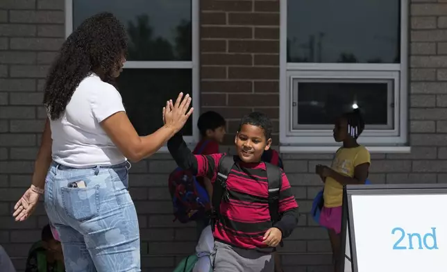 Dylan Martínez-Ramírez, center, high-fives his teacher Aliah James, left, after school Thursday, Aug. 29, 2024, in Aurora, Colo. (AP Photo/Godofredo A. Vásquez)