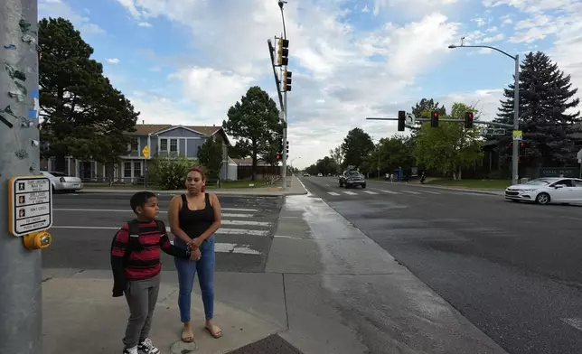 Gabriela Ramírez and her son Dylan wait for the pedestrian signal to cross an intersection on their way to school Thursday, Aug. 29, 2024, in Aurora, Colo. (AP Photo/Godofredo A. Vásquez)