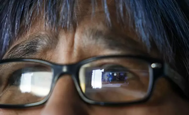 A CBS News broadcast showing Democratic presidential nominee Vice President Kamala Harris is reflected in the eyeglasses of Alice Aishanna as she watches television at her home in Kaktovik, Alaska, Tuesday, Oct. 15, 2024. (AP Photo/Lindsey Wasson)