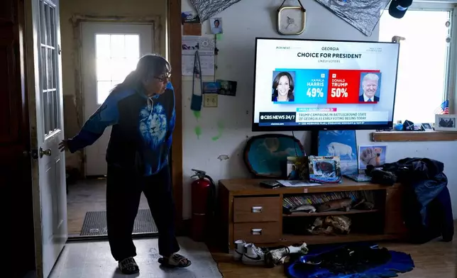 Alice Aishanna steps into her living room while a CBS News broadcast shows Democratic presidential nominee Kamala Harris and Republican presidential nominee former President Donald Trump, Tuesday, Oct. 15, 2024, at her home in Kaktovik, Alaska. (AP Photo/Lindsey Wasson)