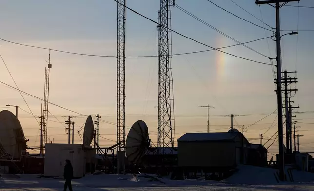 A sundog forms a vertical rainbow as a villager walks by transmission dishes in Kaktovik, Alaska, Tuesday, Oct. 15, 2024. (AP Photo/Lindsey Wasson)