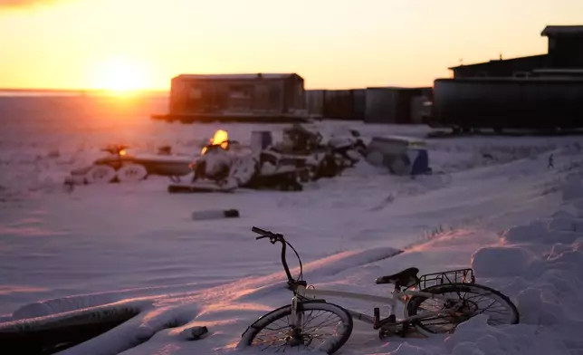 The sun rises over a bicycle covered in snow at the edge of the village in Kaktovik, Alaska, Tuesday, Oct. 15, 2024. (AP Photo/Lindsey Wasson)