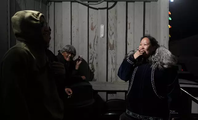 Kitty Ahvakana, right, takes a smoke break with other villagers during a "singspiration" gathering on the porch of the community center in Kaktovik, Alaska, Monday, Oct. 14, 2024. (AP Photo/Lindsey Wasson)