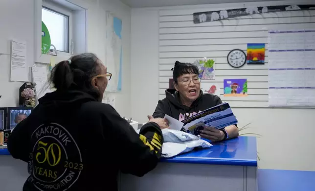 Postmaster Angel Akootchook, the village's only full-time postal employee, hands a stack of mail to a resident in Kaktovik, Alaska, Wednesday, Oct. 16, 2024. (AP Photo/Lindsey Wasson)