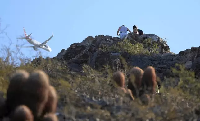 Hikers climb "A" Mountain as a passenger jet flies over Tuesday, Sept. 24, 2024, in Tempe, Ariz. (AP Photo/Ross D. Franklin)