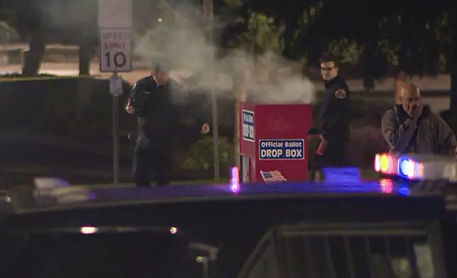 In this image made from a video provided by KGW8, authorities investigate smoke pouring out of a ballot box on Monday, Oct. 28, 2024, in Vancouver, Wash. (KGW8 via AP)