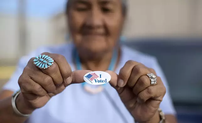 FILE - Mildred James of Sanders, Ariz., shows off her "I Voted" sticker as she waits for results of the Navajo Nation presidential primary election to be revealed in Window Rock, Ariz., Aug. 28, 2018. (AP Photo/Cayla Nimmo, File)