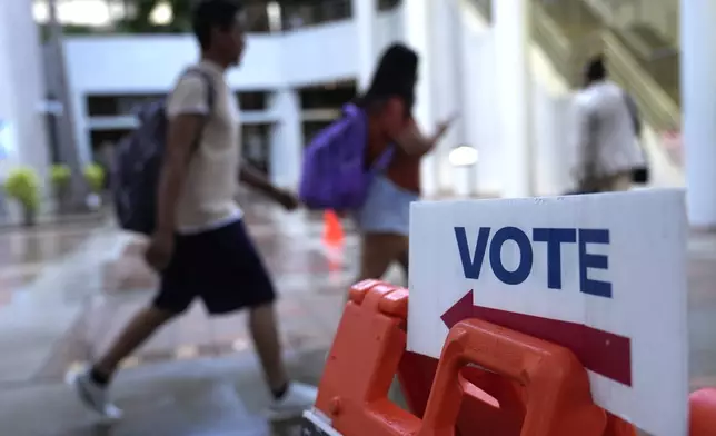 People walk past a Vote sign on the first day of early voting in the general election Monday, Oct. 21, 2024, in Miami. (AP Photo/Lynne Sladky)