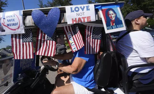 Voters ride in a decorated cart as hundreds of supporters of Democratic presidential nominee Vice President Kamala Harris parade in golf carts to deliver mail-in votes organized by the Villages Democratic Club, in The Villages, Fla., Monday, Oct. 14, 2024. (AP Photo/Rebecca Blackwell)