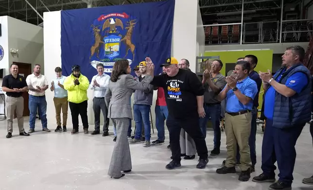 Democratic presidential nominee Vice President Kamala Harris, center left, high-fives a worker as she tours the International Union of Painters and Allied Trades District Council 1M facilities, Monday, Oct. 28, 2024, in Warren, Mich. (AP Photo/Paul Sancya)