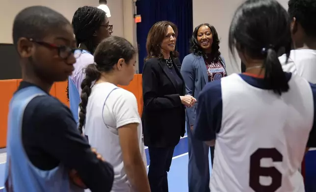 Democratic presidential nominee Vice President Kamala Harris, center, speaks with young basketball players alongide coach Randyll Butler, right, before a community rally at the Alan Horwitz "Sixth Man" Center, Sunday, Oct. 27, 2024, in Philadelphia. (AP Photo/Susan Walsh)