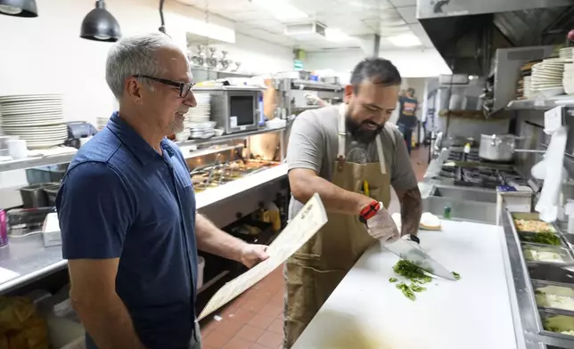 Dan Piacquadio, left, owner of Harold's Cave Creek Corral, waits to talk with chef and kitchen manager Lucio Osorno as he works in the kitchen as Piacquadio waits for the upcoming election and the results of Arizona Prop 138 on minimum wage Thursday, Oct. 3, 2024, in Cave Creek, Ariz. (AP Photo/Ross D. Franklin)