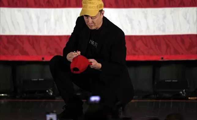 Elon Musk signs as Philadelphia Phillies hat as he speaks as part of a campaign town hall in support of Republican presidential nominee former President Donald Trump in Folsom, Pa., Thursday, Oct. 17, 2024. (AP Photo/Matt Rourke)