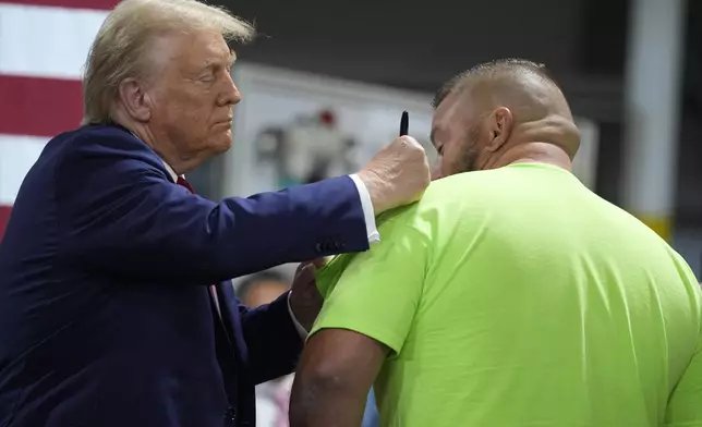 Republican presidential nominee former President Donald Trump autographs a short after speaking at a campaign roundtable, Friday, Oct. 18, 2024, in Auburn Hills, Mich. (AP Photo/Evan Vucci)