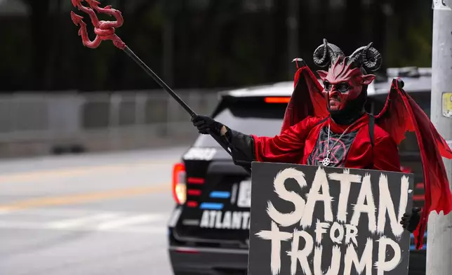 A demonstrator speaks as vehicles move by near a venue where former President Donald Trump will be speaking ahead of an election rally, Monday, Oct. 28, 2024, in Atlanta, Ga. (AP Photo/Mike Stewart)