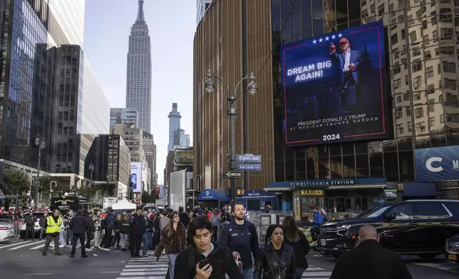 People walk past video boards displaying information about the campaign rally for Republican presidential nominee former President Donald Trump outside Madison Square Garden, Sunday, Oct. 27, 2024, in New York. (AP Photo/Yuki Iwamura)