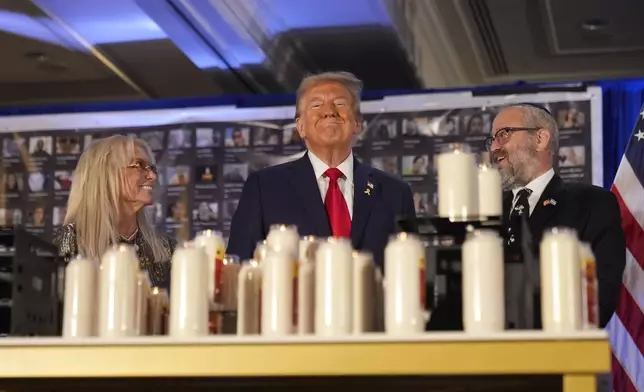 Republican presidential nominee former President Donald Trump stands with Miriam Adelson and Rabbi Yeshuda Kaploun at an event marking one year since the Oct. 7 Hamas attack on Israel, Monday, Oct. 7, 2024, in Miami. (AP Photo/Alex Brandon)