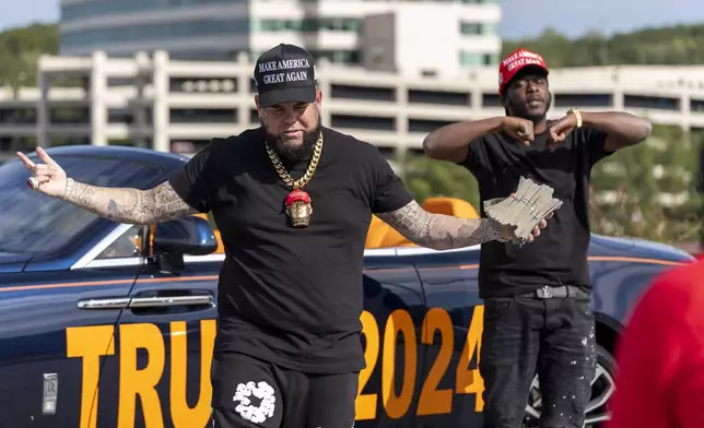 Forgiato Blow, left, and Therealblackdonaldtrump film a music video in the parking lot before Republican presidential nominee former President Donald Trump speaks at a campaign event at the Cobb Energy Performing Arts Centre, Tuesday, Oct. 15, 2024, in Atlanta. (AP Photo/Alex Brandon)