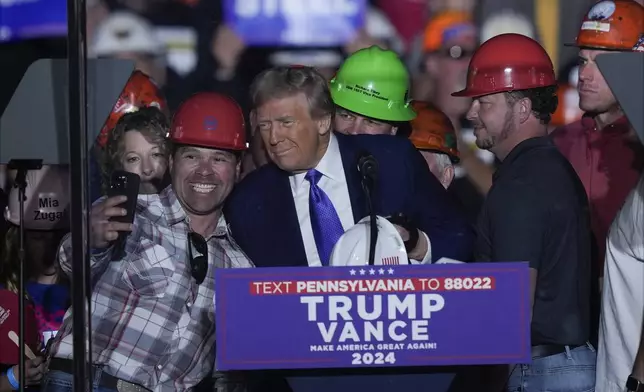 Republican presidential nominee former President Donald Trump poses for a photo as he brings steelworkers onto stage as he speaks at a campaign rally, Saturday, Oct. 19, 2024, at Arnold Palmer Regional Airport in Latrobe, Pa. (AP Photo/Matt Rourke)