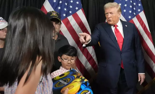 Republican presidential nominee former President Donald Trump, right, gifts a young attendee a pair of shoes before he speaks at a campaign rally at the Calhoun Ranch, Saturday, Oct. 12, 2024, in Coachella, Calif. (AP Photo/Alex Brandon)